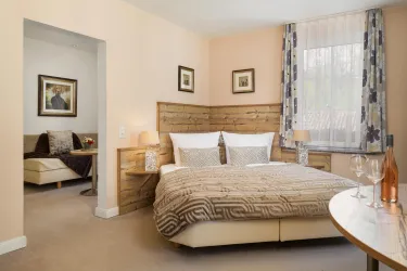 Ein gemütliches Schlafzimmer mit einem großen Bett und weichen Kissen. Im Hintergrund befindet sich ein Wohnbereich mit einem gemütlichen Sofa.