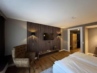 Ein modernes Hotelzimmer mit einem bequemen Sessel und einer Holzverkleidung an der Wand. Der Raum ist hell und gut ausgestattet mit einem Fernseher und einem Holzregal.