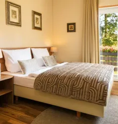 Ein gemütliches Schlafzimmer mit einem großen Bett und dekorativen Kissen. Große Fenster lassen viel Tageslicht herein und bieten einen Blick auf die Natur.