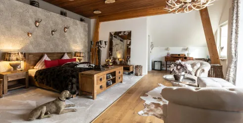 Ein elegantes Schlafzimmer mit Holzmöbeln und einem großen Bett. Ein Hund liegt entspannt auf dem Boden, während die stilvolle Einrichtung eine gemütliche Atmosphäre schafft.