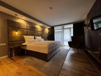 Ein modernes Schlafzimmer mit einem großen Bett und sanfter Beleuchtung. Die Holzböden und der stilvolle Sessel schaffen eine angenehme Atmosphäre.