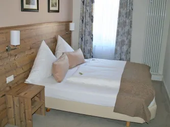 Ein gemütliches Schlafzimmer mit einem Doppelbett und einer Holzverkleidung. Der Raum ist hell und freundlich, mit sanften Farben und Fensterblick.