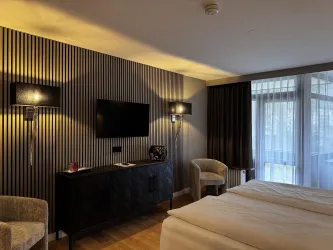 Ein modernes Hotelzimmer mit zwei Einzelbetten und eleganten Stühlen. Die Einrichtung ist stilvoll mit Holzfußboden und großen Fenstern für viel Tageslicht.