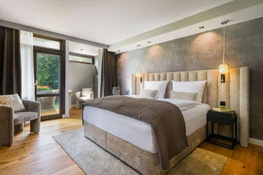 Ein modernes Schlafzimmer mit einem großen Bett und gemütlicher Einrichtung. Helle Farben und ein Fenster bieten einen Blick ins Freie.