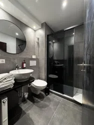 Ein modernes Badezimmer mit grauen Wänden und Fliesen. Es verfügt über eine Dusche, ein Waschbecken und frische Handtücher.