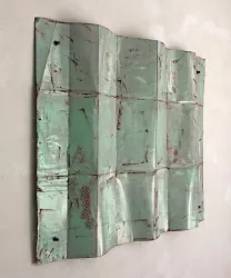 Ein großes, bemaltes Metallstück hängt an der Wand. Es hat eine rostige, grüne Patina und interessante geometrische Muster.