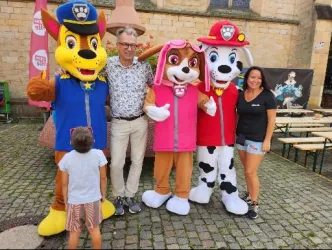 Eine Gruppe von vier Personen steht zusammen, darunter zwei Erwachsene und zwei Kinder. Die Erwachsenen sind in bunten Kostümen von Kindheitshelden bekleidet, umgeben von einer fröhlichen Atmosphäre.