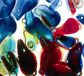 Bunte Glasstücke in Blau, Rot und Gelb liegen übereinander. Die Lichtdurchlässigkeit erzeugt einen faszinierenden, kaleidoskopartigen Effekt.
