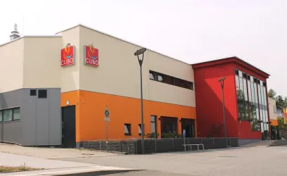 Ein modernes Gebäude mit bunten Außenwänden in Orange und Rot. An der Fassade befinden sich die Schilder des Unternehmens "CUBO".