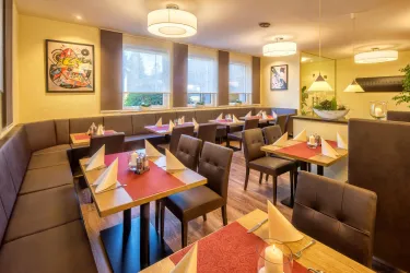 Ein elegantes Restaurant mit gemütlichen Sitzbereichen und modernen dekorativen Elementen. Die Tische sind sorgfältig gedeckt und schaffen eine einladende Atmosphäre.