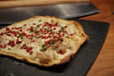 Ein frisch gebackenes Flammkuchen mit Zwiebeln, Speck und Schnittlauch. Der Teig ist knusprig und goldbraun.