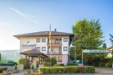 Ein einladendes Gebäude mit einem Restaurant und einem Biergarten. Umgeben von grünen Bäumen und einem klaren Himmel.