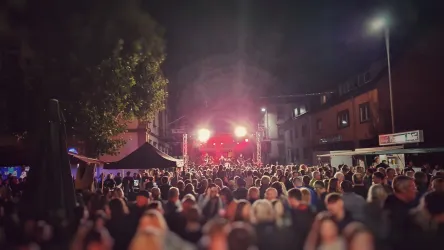 Eine große Menschenmenge bei einem Nachtfestival mit bunten Lichtern auf der Bühne. Die Atmosphäre ist festlich und lebhaft.