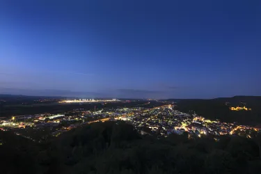 Eine atemberaubende Aussicht auf eine Stadt bei Nacht, beleuchtet von vielen Lichtern. Der Himmel ist dunkelblau und die Umgebung ist bergig.