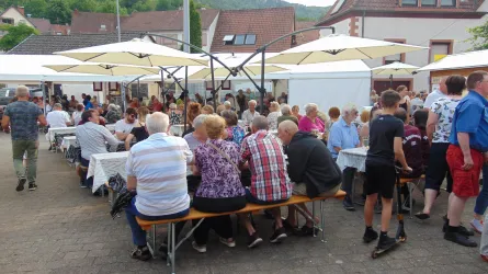 Wuseliges Treiben auf dem Festplatz. Besucher sitzen auf Bierbänken an Tischen.