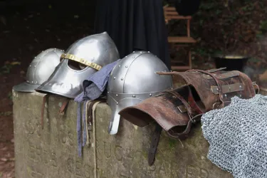 Ein Steinsockel, auf dem  mehrere mittelalterliche Ritterhelme und Rüstungsteilen.