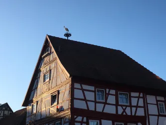 Ein traditionelles Fachwerkhaus mit einem steilen Dach und einem großen Wetterhahn. Der Himmel ist klar und blau.