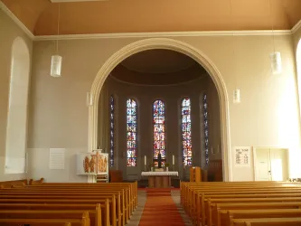 Innenansicht der Stadtkirche Annweiler. Im Vordergrund Bankreihen mit Mittelgang. Im Hintergrund Altar mit bunten Fenstern.