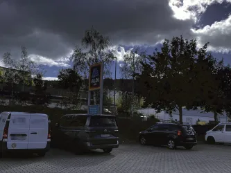 Ein Aldi-Supermarkt mit Parkplatz. Der Himmel ist bewölkt und es stehen mehrere Autos in der Nähe.