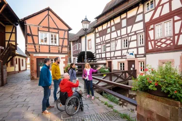 Eine Gruppe von fünf Personen steht in einer malerischen, engen Gasse mit Fachwerkhäusern. Sie scheinen sich angeregt zu unterhalten und die Umgebung zu erkunden.