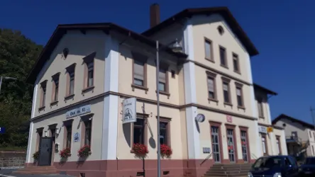 Ein altes Wohngebäude mit einer klassischen Architektur. Die Fassade ist hellgelb mit braunen Akzenten und Blumenkästen.