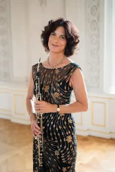 Eine elegante Frau steht in einem geschmackvoll dekorierten Raum. Sie hält ein Oboe und trägt ein schönes, verziertes Kleid.