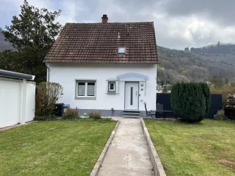 Ein charmantes Einfamilienhaus mit einem gepflegten Garten und einem gepflasterten Weg. Im Hintergrund sind sanfte Hügel zu sehen.