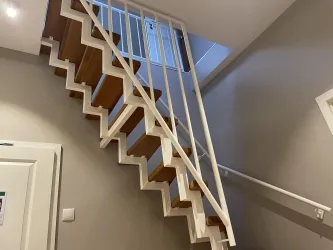 Eine moderne Treppe mit Holzstufen und einem weißen Geländer. Der Raum hat helle Wände und viel natürliches Licht.