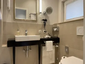 Ein modernes Badezimmer mit einem Waschbecken und einem großen Spiegel. Die Wände sind in neutralen Farbtönen gehalten und es gibt einige grundlegende Annehmlichkeiten.