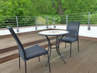 Ein gemütlicher Balkon mit einem kleinen Tisch und zwei Stühlen. Umgeben von grünen Bäumen bietet der Platz eine entspannte Atmosphäre.