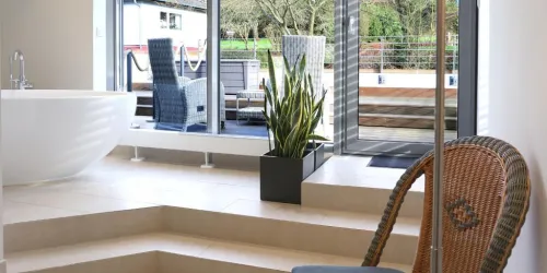 Ein modernes Badezimmer mit einer großen freistehenden Badewanne und einem Blick auf einen Außenbereich. Grüne Pflanzen und stilvolle Möbel schaffen eine entspannende Atmosphäre.