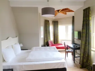 Ein modernes Hotelzimmer mit zwei Betten und großen Fenstern. Im Raum befinden sich ein Tisch, ein Fernseher und eine rote Couch.