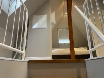 Ein heller und einladender Treppenaufgang mit einer weißen Geländer. Oben ist ein Schlafzimmer mit einem Bett und einem Fenster sichtbar.