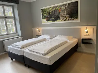 Ein gemütliches Schlafzimmer mit zwei Einzelbetten und einem klaren Design. An der Wand hängt ein großes Bild, das eine natürliche Szene zeigt.