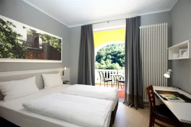Ein modernes Hotelzimmer mit zwei Einzelbetten und einem Schreibtisch. Der Raum hat große Fenster, die einen Blick auf die grüne Landschaft bieten.
