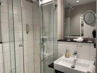 Ein modernes Badezimmer mit einer Glasdusche und einem eleganten Waschbecken. Die Wände sind hell gefliest und es gibt eine große Spiegelwand.