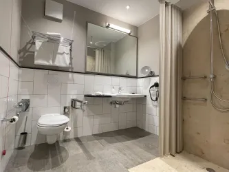 Ein modernes Badezimmer mit einer Dusche, einem Waschbecken und einem WC. Die Wände sind hell gefliest und ein großer Spiegel sorgt für zusätzlichen Komfort.