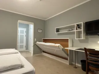 Ein einfaches Zimmer mit zwei Betten und einem ausklappbaren Bett. An der Wand befindet sich ein Fernseher und ein Schreibtisch.