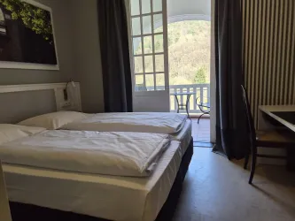 Ein helles Zimmer mit zwei Einzelbetten und einem Tisch. Durch die Fenster sieht man einen schönen Ausblick auf die Natur.