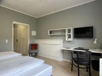 Ein gemütliches Hotelzimmer mit zwei Betten und einem Schreibtisch. An der Wand befindet sich ein Fernseher und eine sitzgelegenheit in der Ecke.