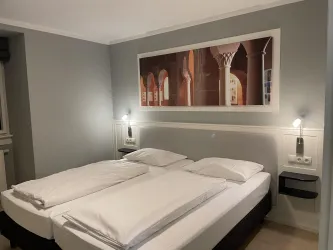 Ein modernes Schlafzimmer mit zwei Einzelbetten und einer minimalistischen Einrichtung. An der Wand hängt ein großes Bild mit architektonischen Motiven.