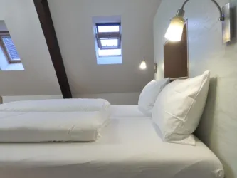 Ein helles Zimmer mit schrägen Wänden und zwei bequemen Betten. Die Fenster lassen viel natürliches Licht herein und sorgen für eine angenehme Atmosphäre.