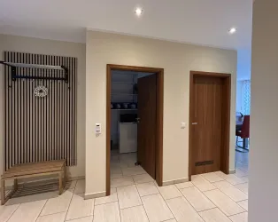 Ein heller Flur mit zwei Holz-Türen und einem modernen Schrank. An der Wand befindet sich eine Garderobe und der Boden ist gefliest.
