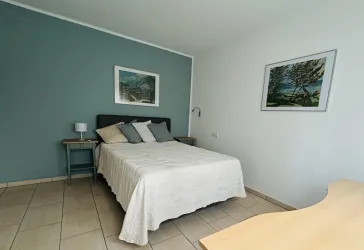 Ein modernes Schlafzimmer mit einem großen Bett und dekorativen Kissen. An der Wand hängt ein Bild und der Raum ist in sanften Farben gestaltet.