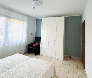 Ein ruhiges Schlafzimmer mit einem Doppelbett und einem weißen Kleiderschrank. An einer Wand steht ein schwarzer Sessel und viel Tageslicht fällt durch das Fenster.