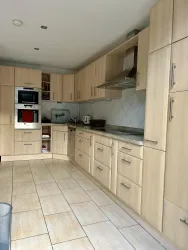 Eine moderne Küche mit hellen Holzschränken und einer großzügigen Arbeitsfläche. Die Ausstattung umfasst ein Backofen und eine Spüle sowie große Fliesen auf dem Boden.