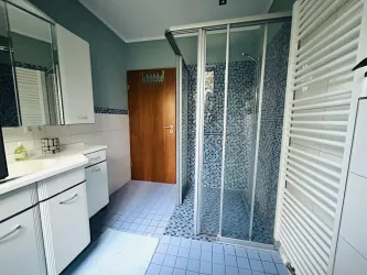 Ein modernes Badezimmer mit einer Duschkabine und hellen Fliesen. Es gibt viel Platz und natürliche Beleuchtung.