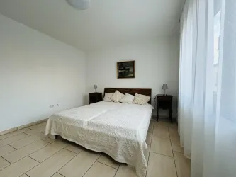 Ein helles Schlafzimmer mit einem großen Bett und einem weißen Bettbezug. Neben dem Bett stehen zwei Nachttische mit Lampen und einem Gemälde an der Wand.