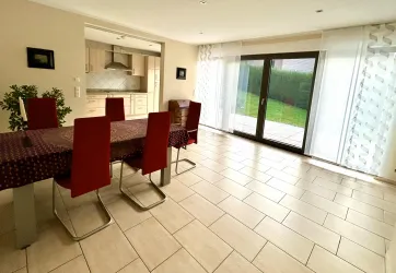 Ein moderner Essbereich mit einem großen Tisch und roten Stühlen. Große Fenster lassen viel Licht herein und bieten einen Blick auf den Garten.