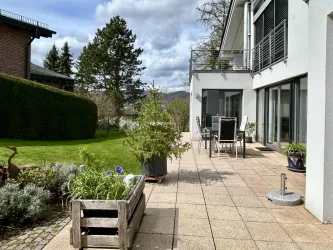 Ein moderner Außenbereich mit einer Terrasse und Gartenmöbeln. Grüne Pflanzen und Blumen tragen zur einladenden Atmosphäre bei.